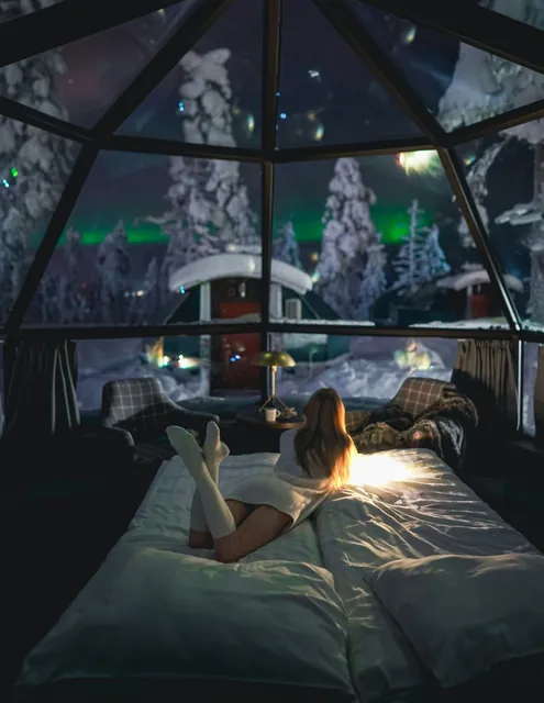 A woman watches the aurora from a bed in a glass igloo in Levi, Finland