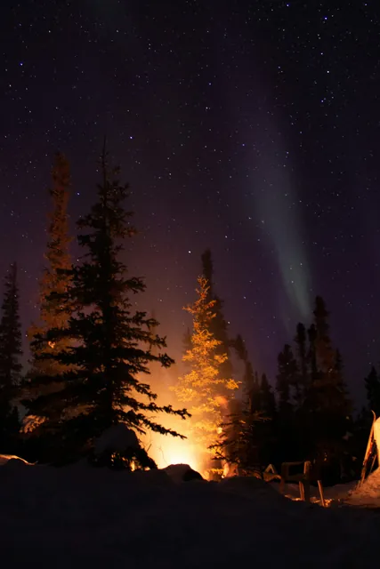 Winter night photography shot of a campfire under the Northern lights just out of Yellowknife, Northwest Territories.