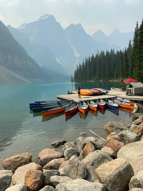 Woman on Pier with Canoes on Lakeshore near Mountains