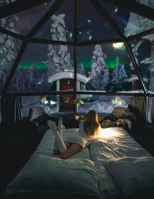A woman watches the aurora from a bed in a glass igloo in Levi, Finland